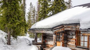 A log cabin with a snow-covered roof, surrounded by snow and trees. - Kelo-ville by Interhome (Sodankylä)