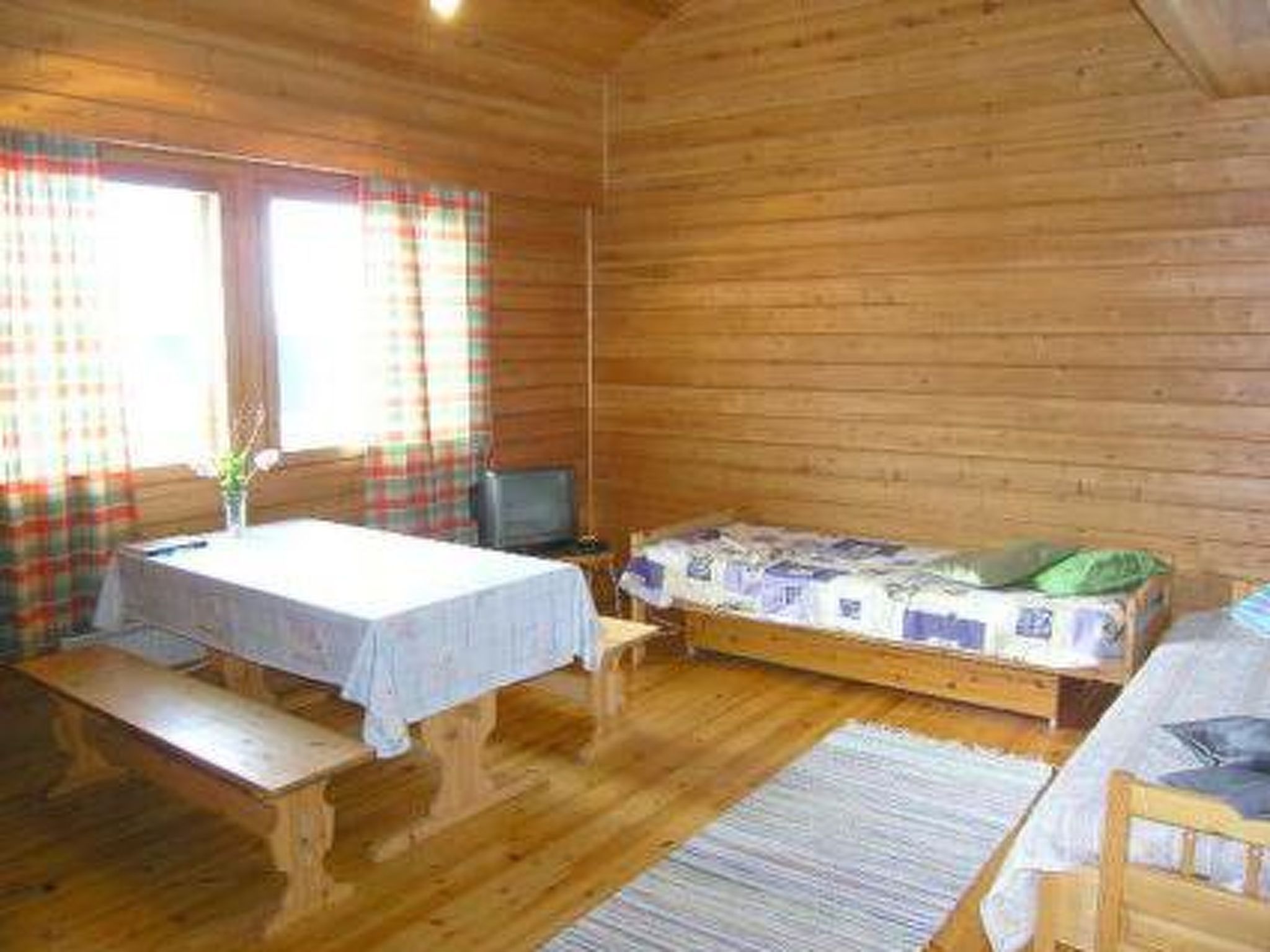 A wooden cabin room with a bed, a small table, and a bench.