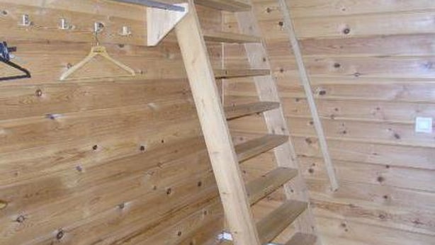 Interior de madera con una escalera y un perchero metálico.