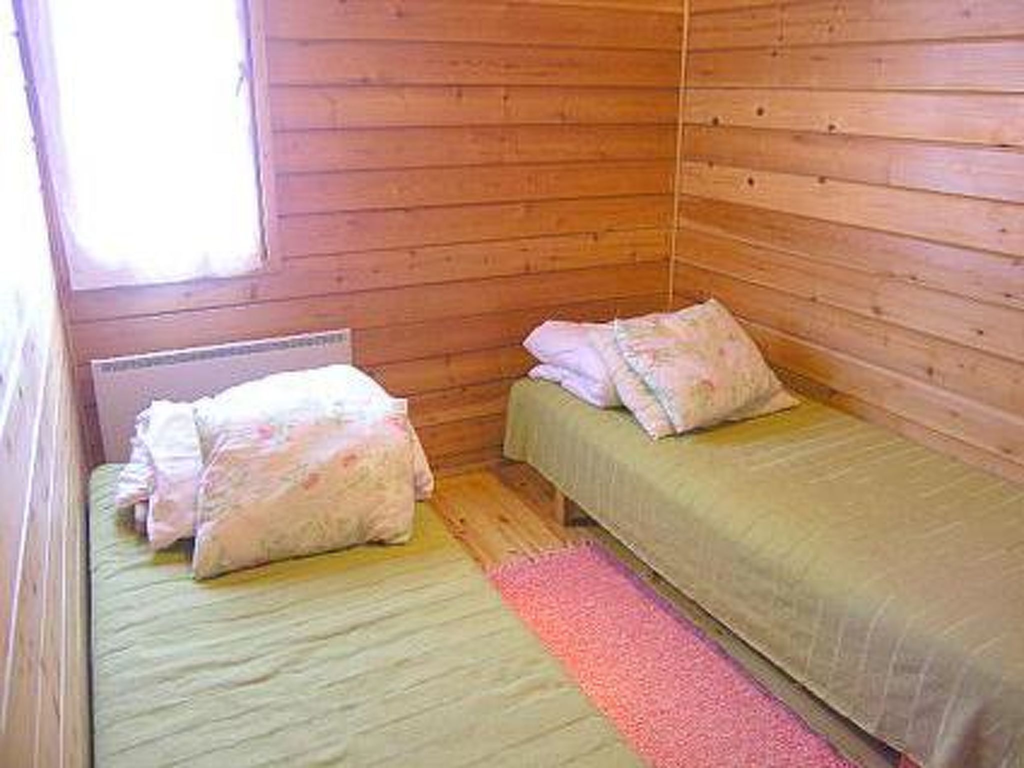 Habitación pequeña con cama individual, paredes de madera y una ventana.