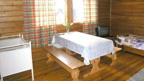 Una habitación tipo cabaña de madera con una cama, una mesa con un florero y cortinas de cuadros.