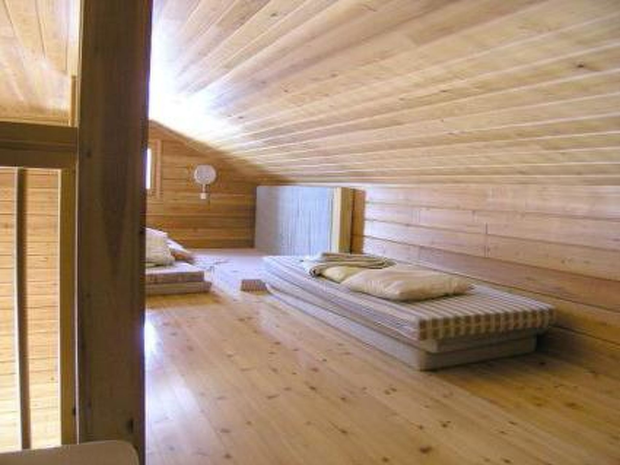 A room with wooden walls and floors, a bed with pillows, and a window.