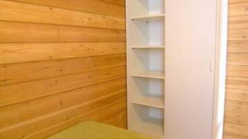 A room with wooden walls, a white wardrobe with multiple shelves, and a green bedspread.