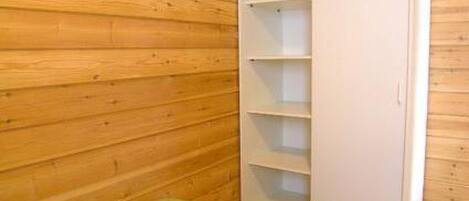 Ein Zimmer mit Holzwänden, einem weißen Kleiderschrank mit mehreren Regalen und einer grünen Bettdecke.