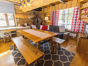 A wooden interior with a dining table, benches, a sofa, and a patterned rug.