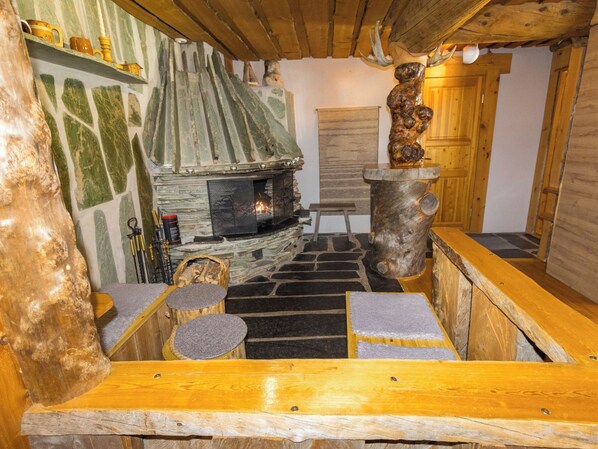 A rustic interior with a stone fireplace, wooden benches, and a wooden sculpture.