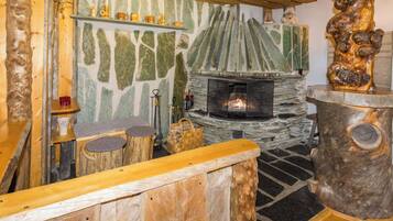 A rustic interior with a stone fireplace, wooden furniture, and a stone wall with greenish patterns.