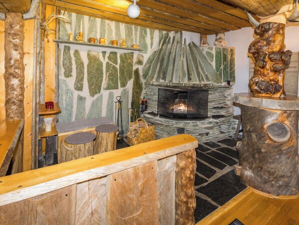 Ein rustikales Interieur mit Kamin aus Stein, Holzmöbeln und einer Steinwand mit grünlichen Mustern.