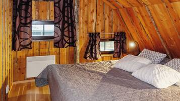A cozy attic bedroom with a bed, two windows, and a heater.