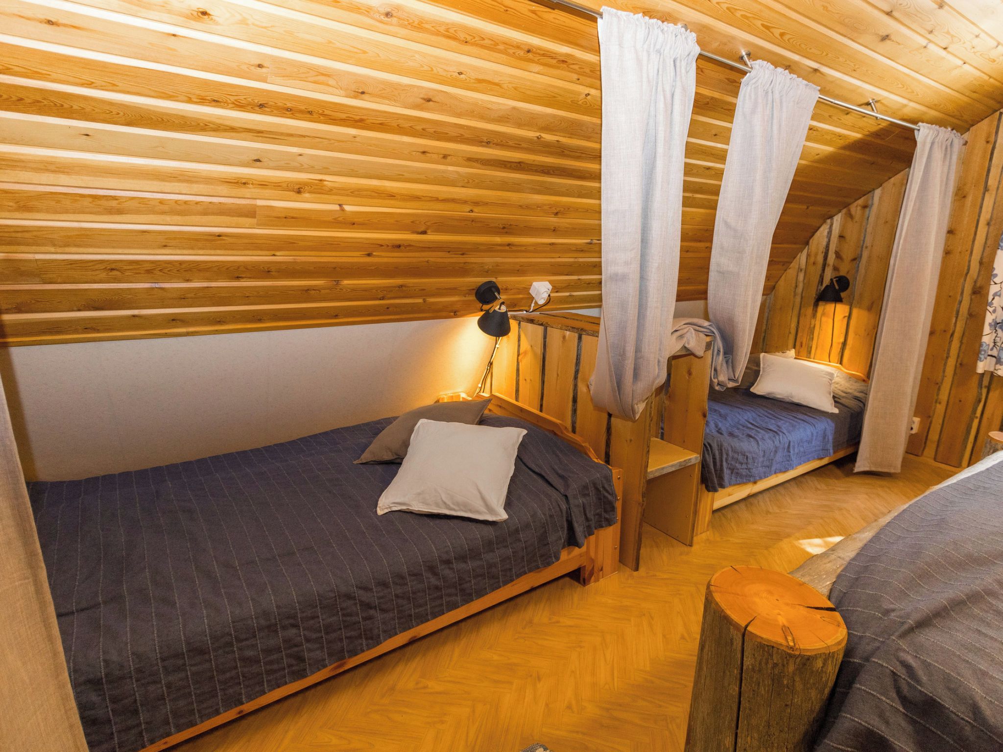 A wooden cabin with two single beds, a small table, and a lamp.