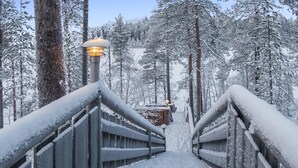 Eine schneebedeckte Holztreppe führt zu einem Gebäude, umgeben von hohen Bäumen.