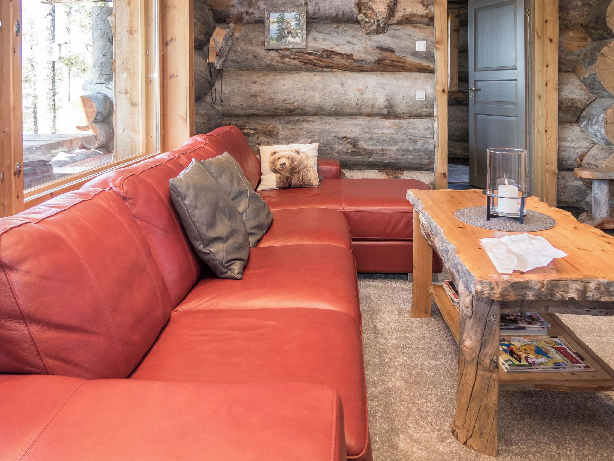 L'intérieur d'une cabane en rondins, avec un canapé en cuir rouge, une table basse en bois et un coussin à motifs d'ours.