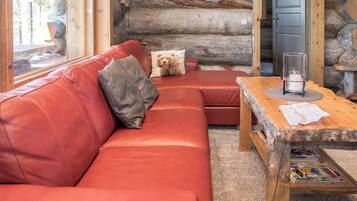 L'intérieur d'une cabane en rondins, avec un canapé en cuir rouge, une table basse en bois et un coussin à motifs d'ours.