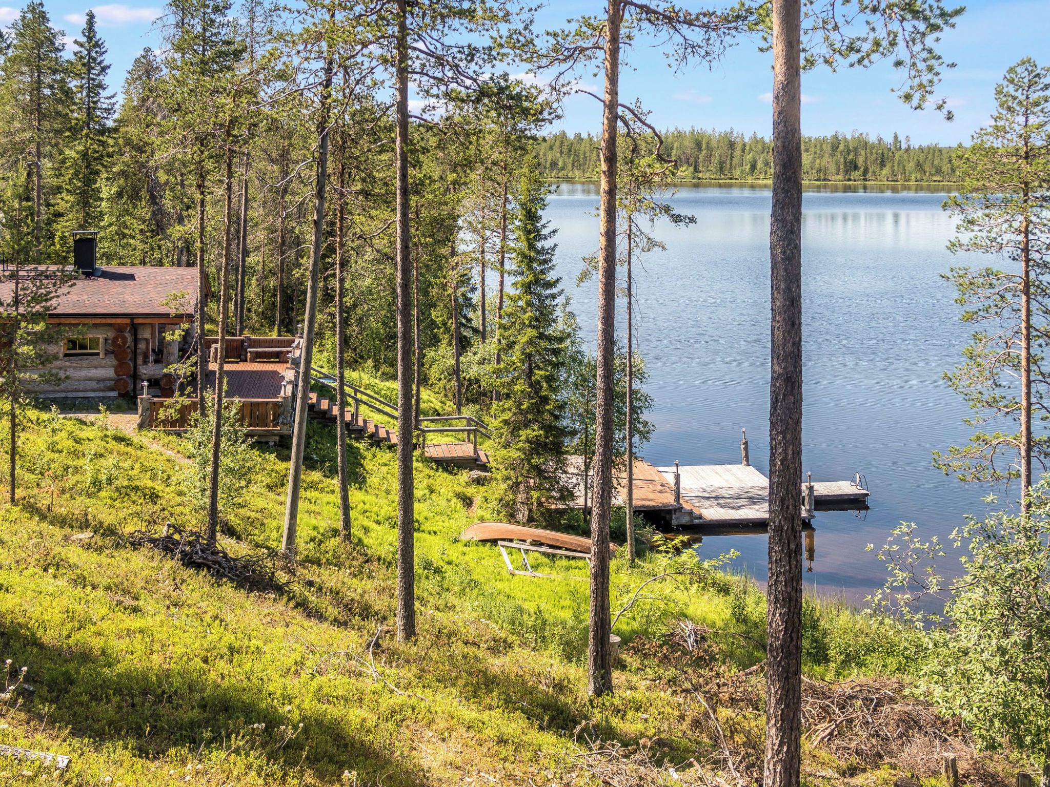 Una cabaña con terraza que da a un lago, rodeada de árboles.