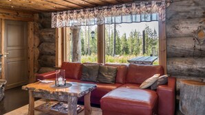 Ein gemütliches Blockhaus-Interieur mit einem Ledersofa, einem rustikalen Couchtisch und Blick auf einen Wald durch große Fenster.