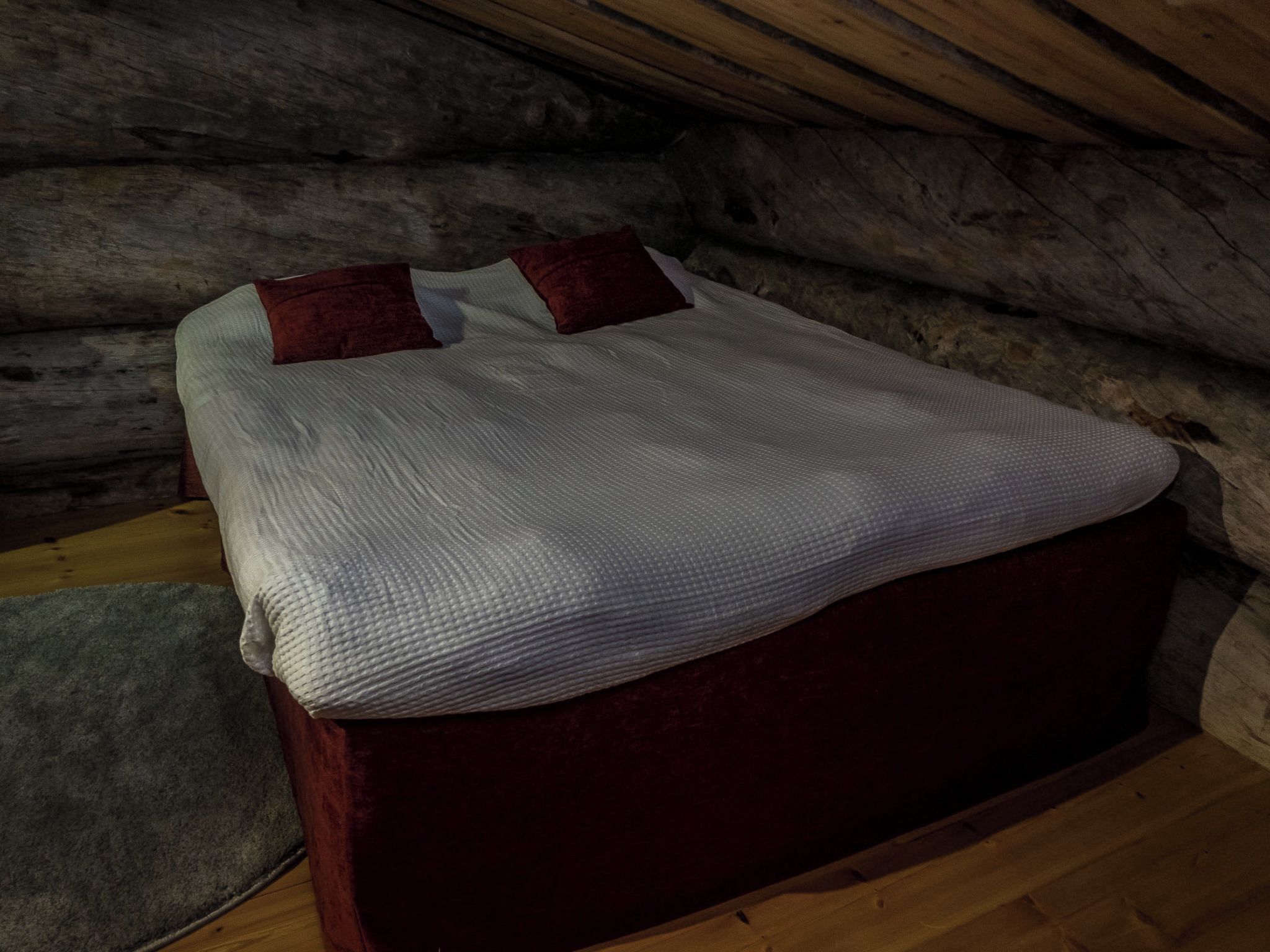 A bed in a log cabin room with a wooden floor and a red headboard.