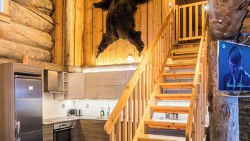A log cabin interior with a kitchen, wooden staircase, and a mounted bear.