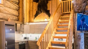 Ein rustikales Blockhaus-Interieur mit einer Holztreppe, einer Küchenzeile und einem aufgehängten Bären an der Wand.