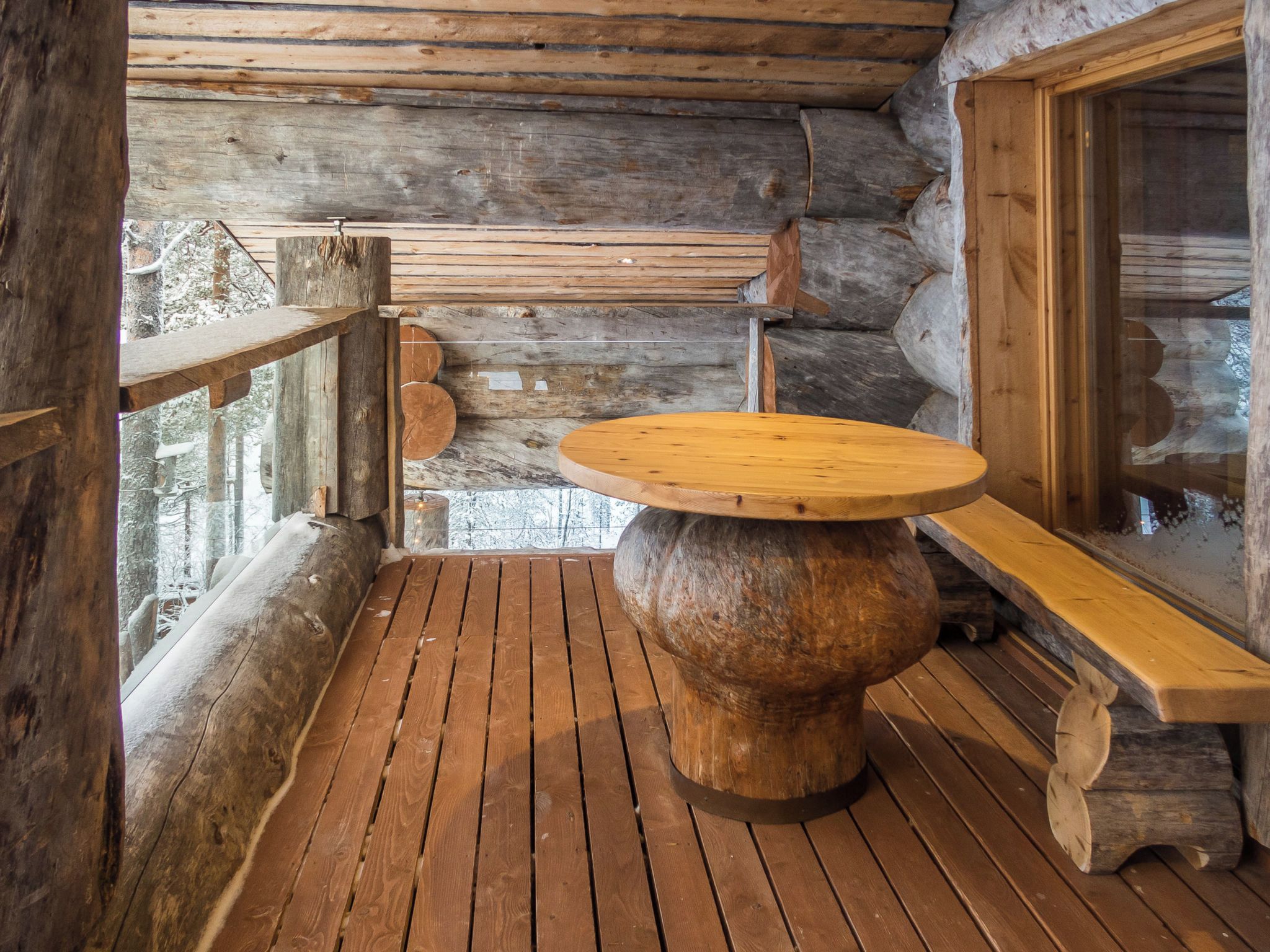 A rustic wooden table with a round top, a bench, and a log wall in the background.