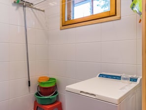 Pieni, siisti kylpyhuone, jossa on valkoiset laatat, ikkuna, pesukone ja pino värikkäitä ämpäreitä.