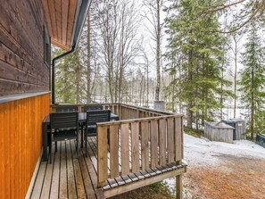 A wooden deck with outdoor seating, surrounded by a forested area with snow on the ground.