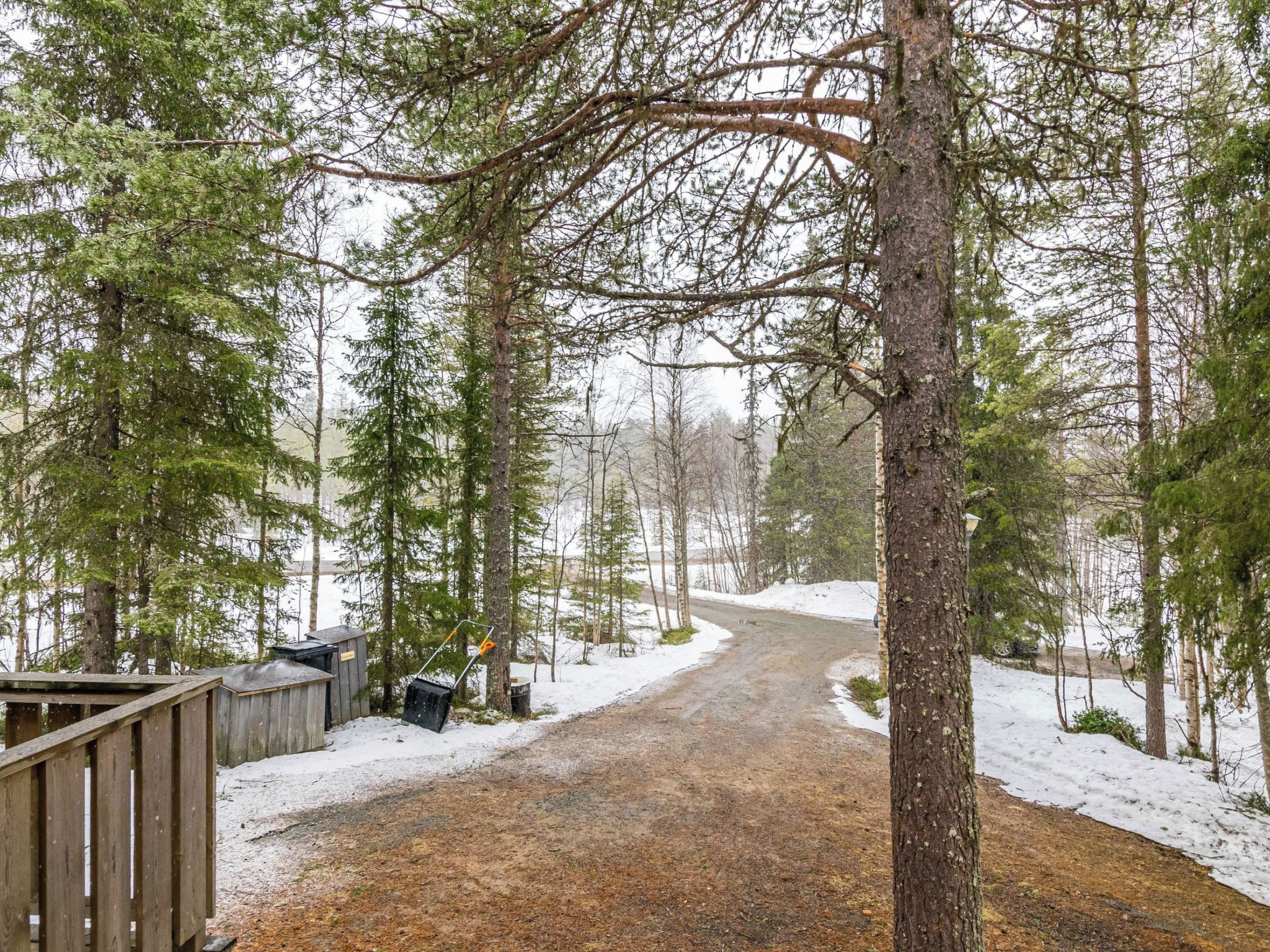 A snow-covered forest path leading to a wooden cabin with a metal snow shovel.