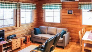 A cozy cabin interior with a sofa, a chair, a small table, and a television on a wooden cabinet. - Ruskatupa by Interhome (Kuusamo)