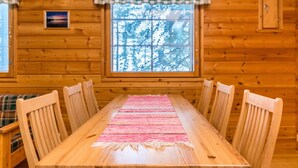 A wooden cabin interior with a dining table, chairs, a window with a view of trees, and plaid curtains. - Ruskatupa by Interhome (Kuusamo)