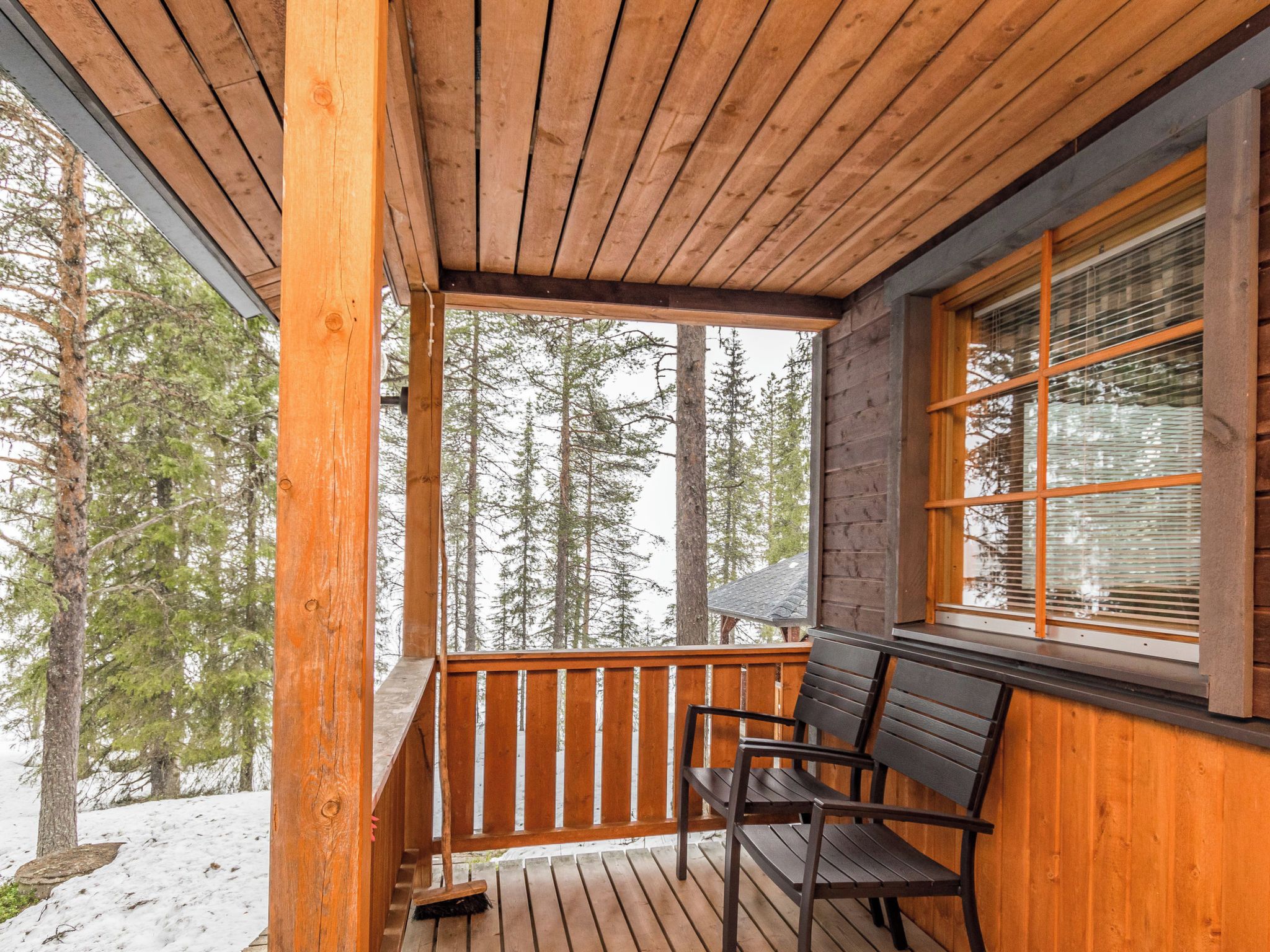 A wooden deck with a railing, a bench, and a window with blinds.