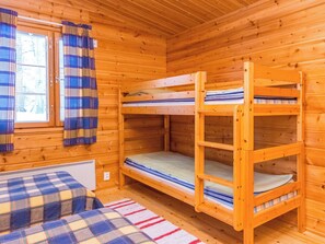 A wooden cabin room with bunk beds, a window with curtains, and a plaid blanket on the floor.