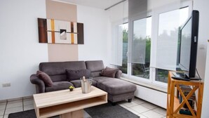 Ein modernes Wohnzimmer mit einem grauen Ecksofa, einem Holztisch und einem Fernseher auf einem Holzgestell.