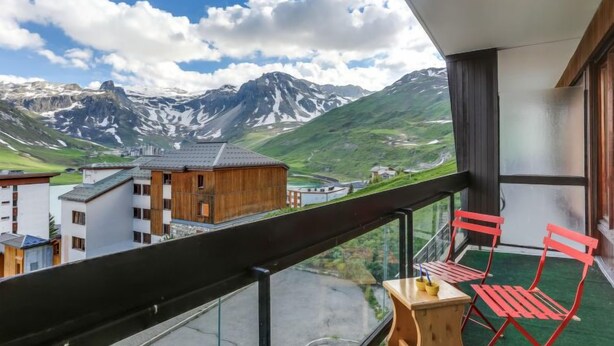 A balcony with a view of mountains and a small building. There are two red chairs and a wooden table. - Le Bec Rouge (Le Lac) by Interhome (Tignes)