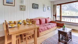 A cozy room with a wooden dining table set with yellow bowls and plates, a pink sofa, and a small wooden table with a bottle and glass. - Le Bec Rouge (Le Lac) by Interhome (Tignes)