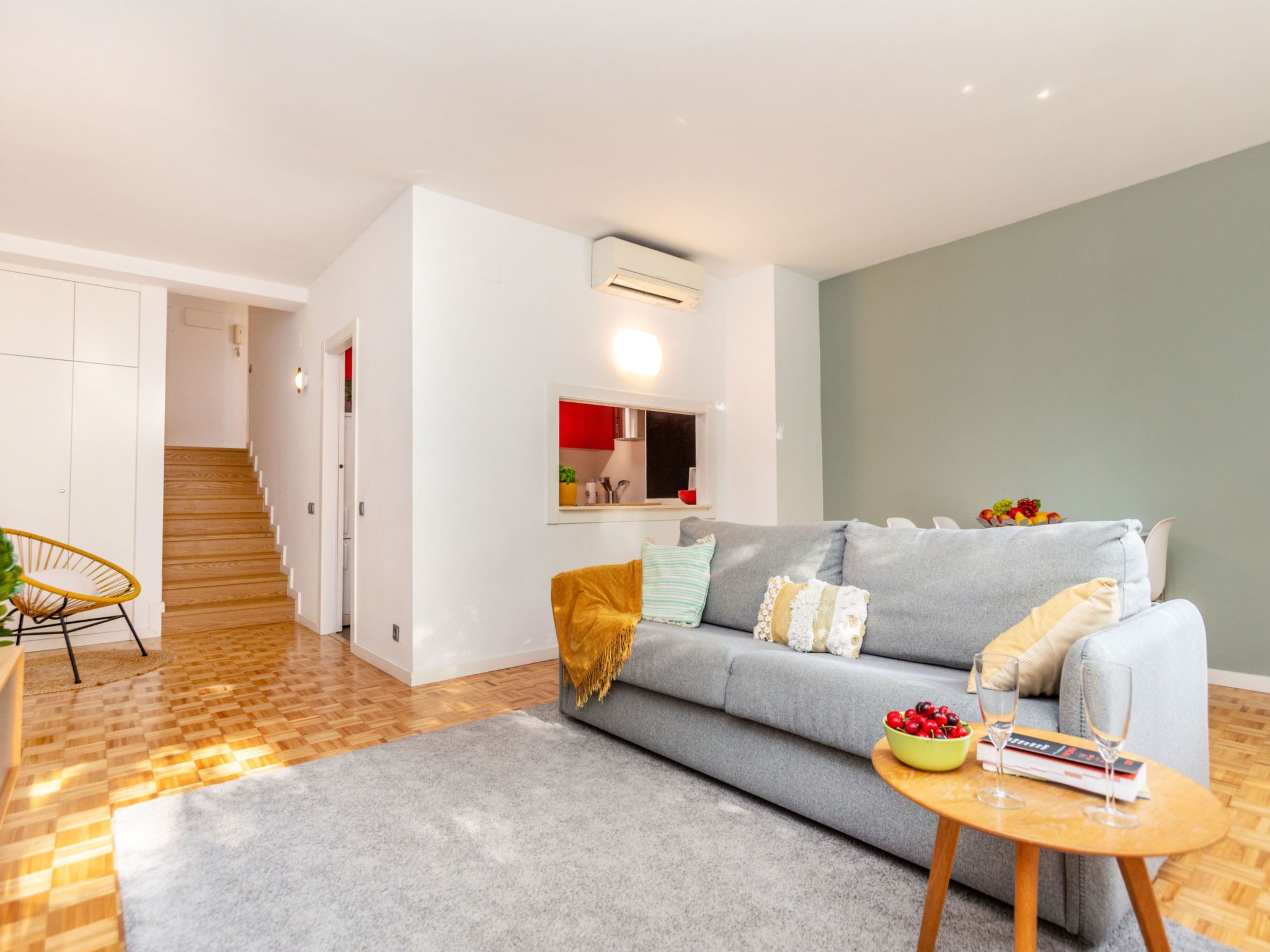 Ein modernes Wohnzimmer mit einem grauen Sofa, Holzboden, einem runden Couchtisch und einer kleinen Essecke mit einem gelben Stuhl.
