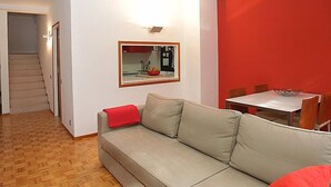Un salon avec un canapé, une table à manger et des chaises, un escalier et un mur d’accent rouge.
