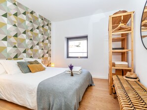 A bedroom with a bed, a wooden wardrobe, a bench, and a geometric-patterned wall.