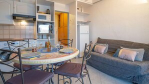 A compact living space with a kitchen area, a dining table with chairs, and a sofa with cushions. - Le Capitole by Interhome (Fréjus)