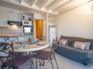 Um espaço de estar compacto com cozinha, mesa de jantar e cadeiras, e sofá com almofadas.