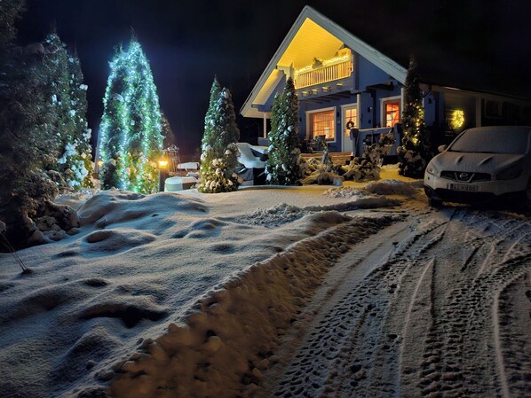 Una strada di accesso innevata che conduce a una casa con portico e luci di Natale.