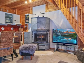 A cozy living room with a stone fireplace, a television, wicker furniture, and a wooden staircase.