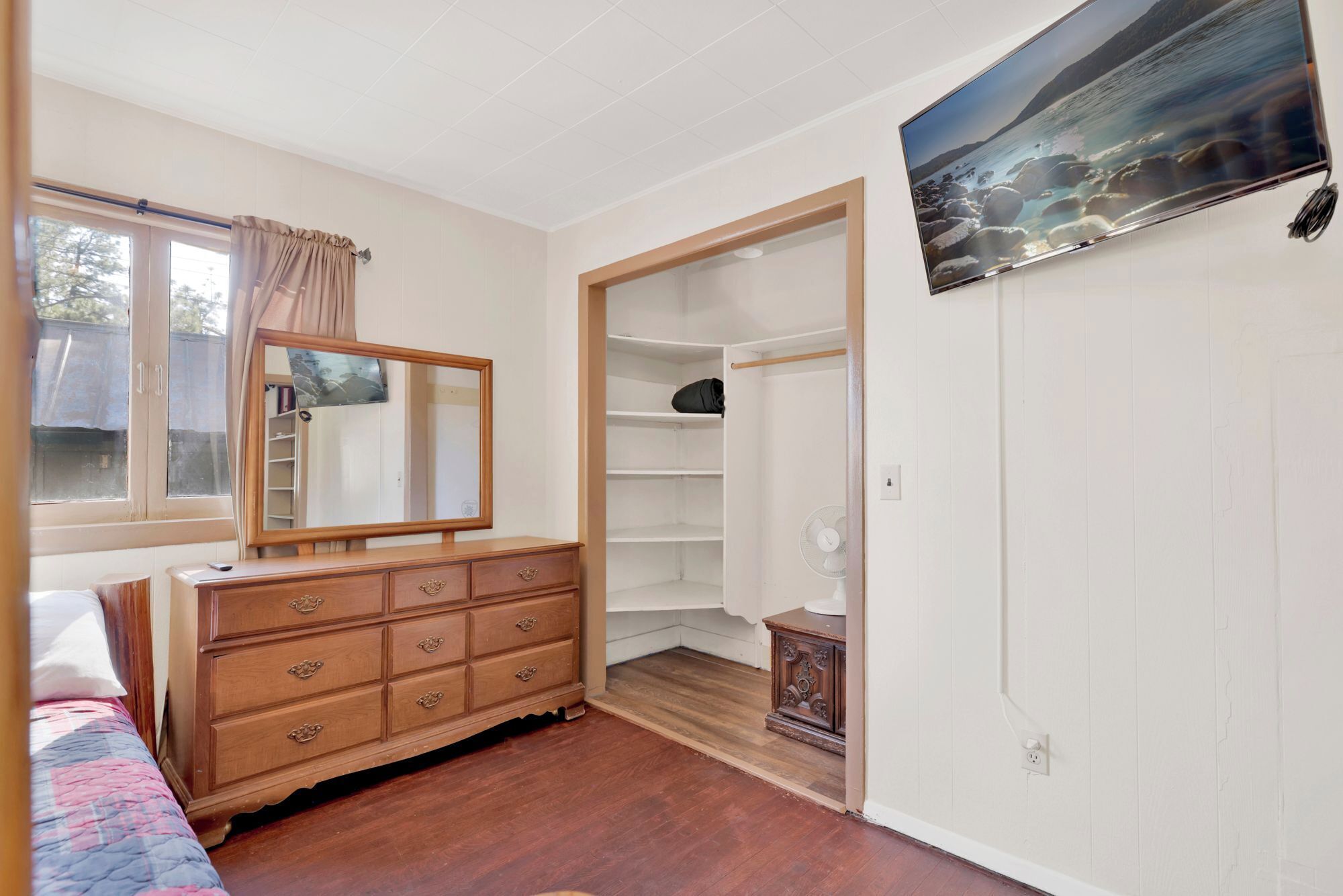 A bedroom with a wooden dresser, a large mirror, a wardrobe, and a painting on the wall.