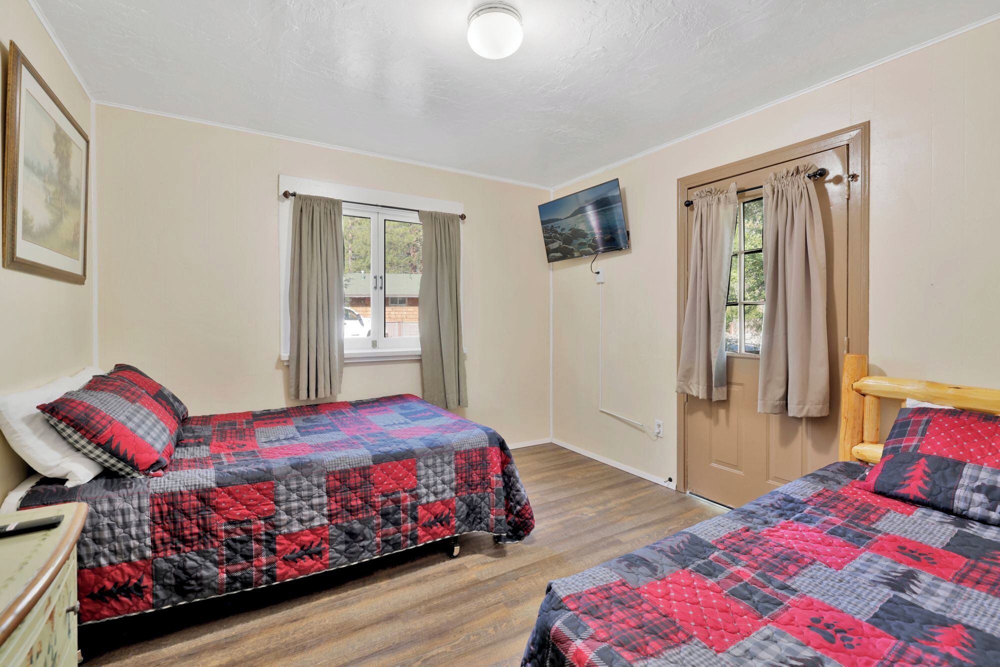 A bedroom with two beds, a TV mounted on the wall, and a wooden dresser.