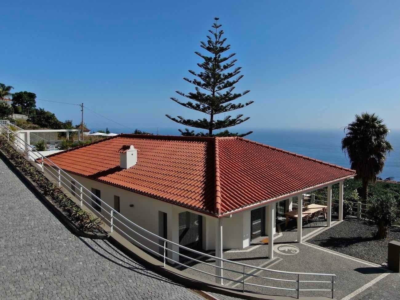 A building with a red-tiled roof, a covered patio with seating, and a view of the sea.