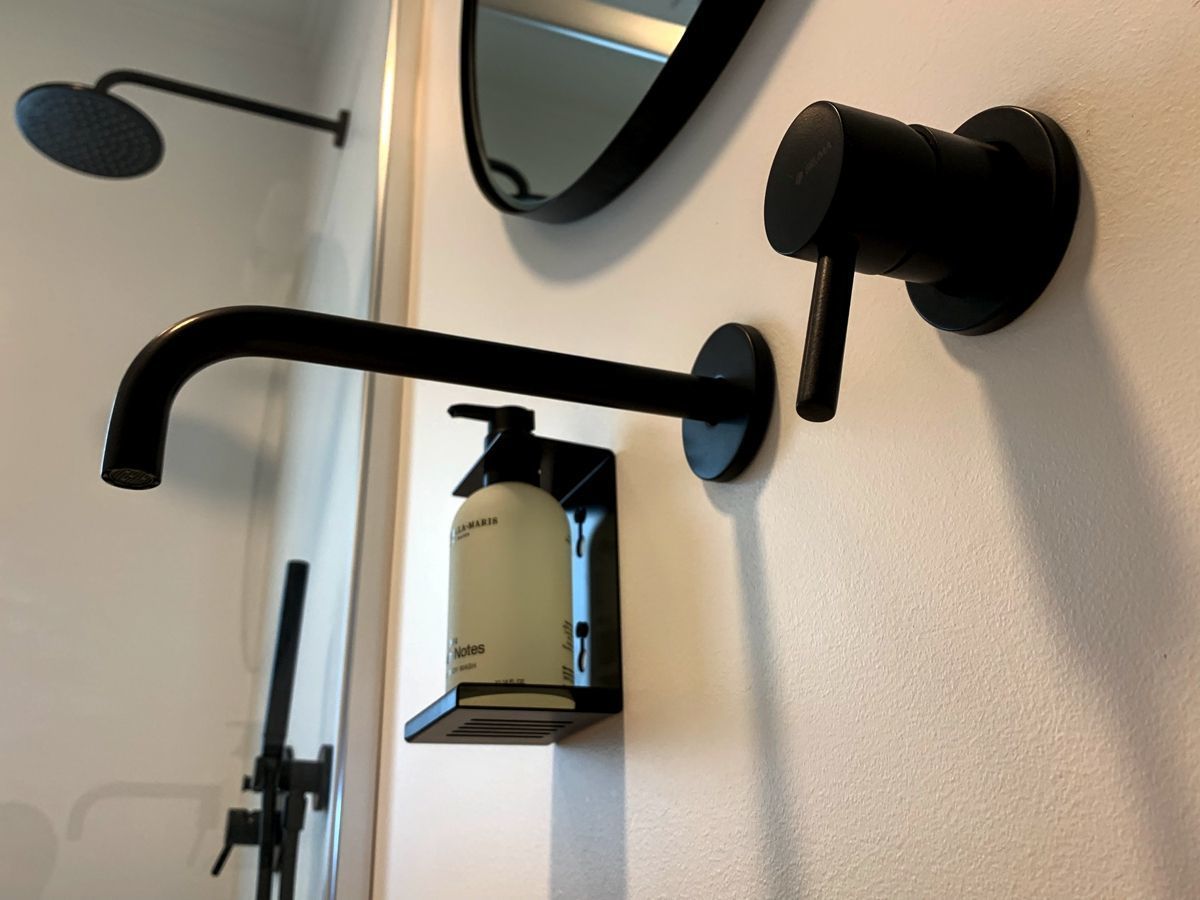 Een badkamer met een zwarte handdoekhouder, een handzeepdispenser en een spiegel.