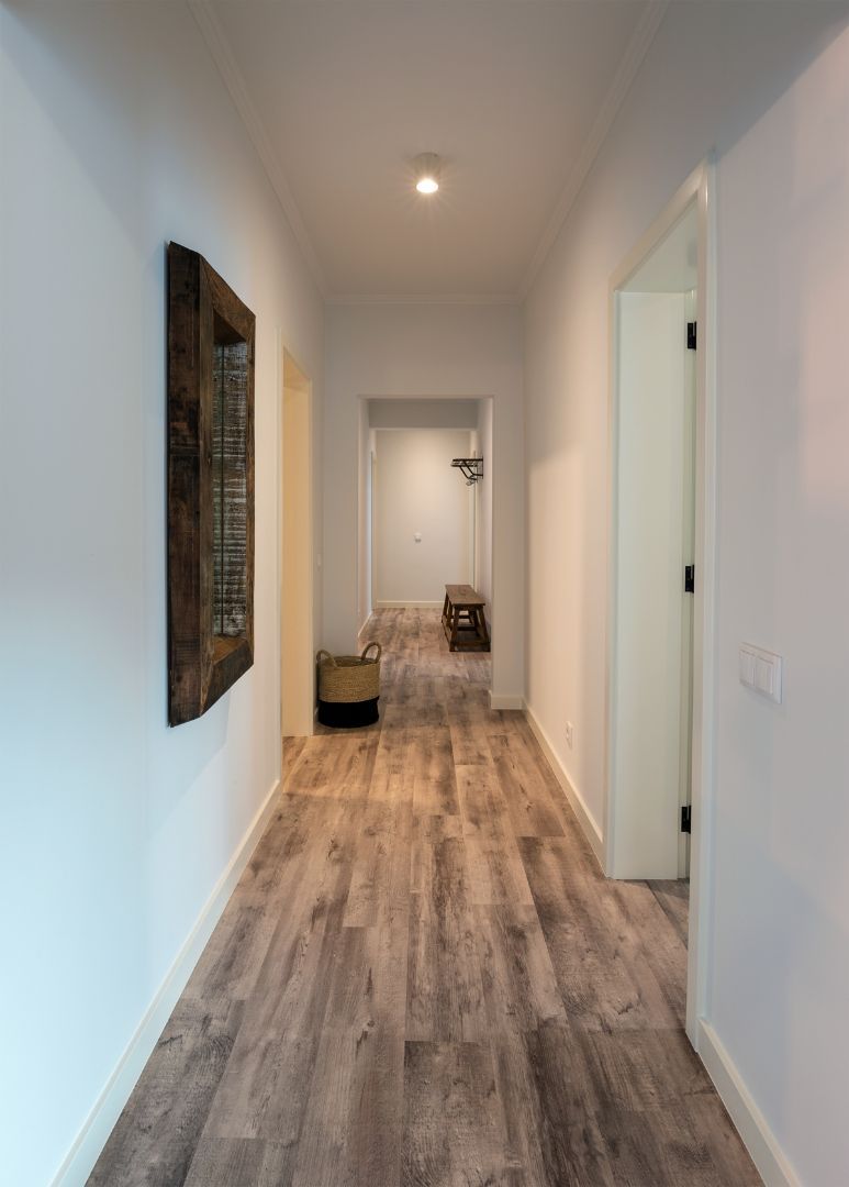 Un pasillo con suelo de madera, una cesta colgante y una puerta al final.