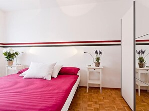 Een slaapkamer met een bed, twee nachtkastjes met plantenpotten, een spiegel en een muur met rode strepen.