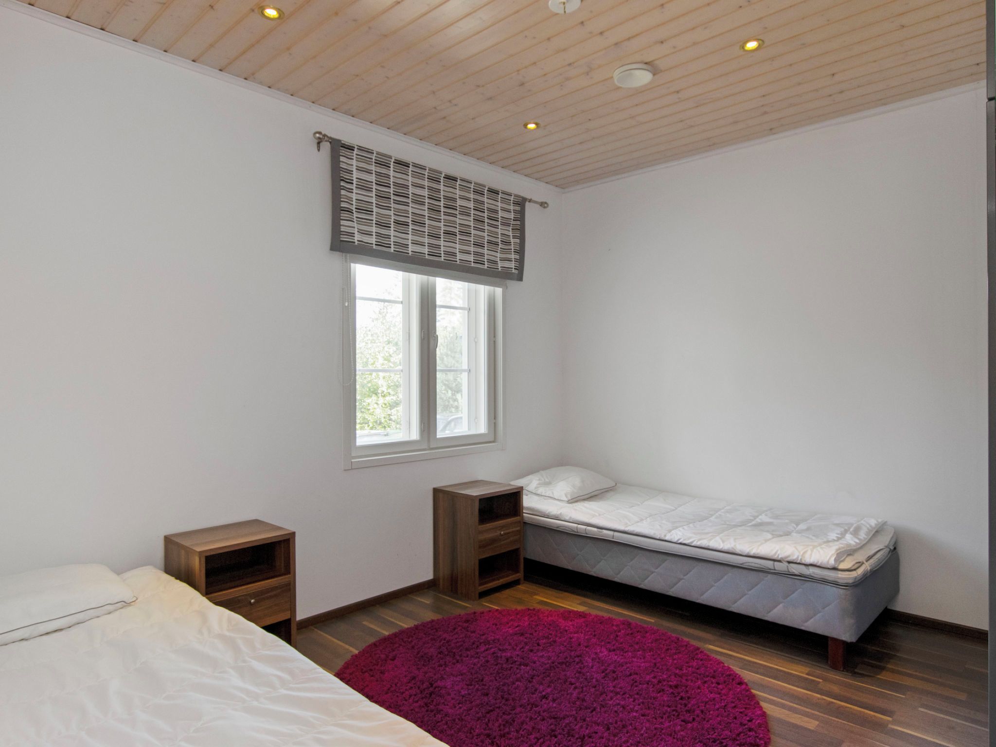 Un dormitorio con cama, ventana, mesita de noche y una alfombra morada.