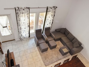 Un salon comprenant un canapé d’angle, des poufs, un tapis et un coin repas avec des chaises.