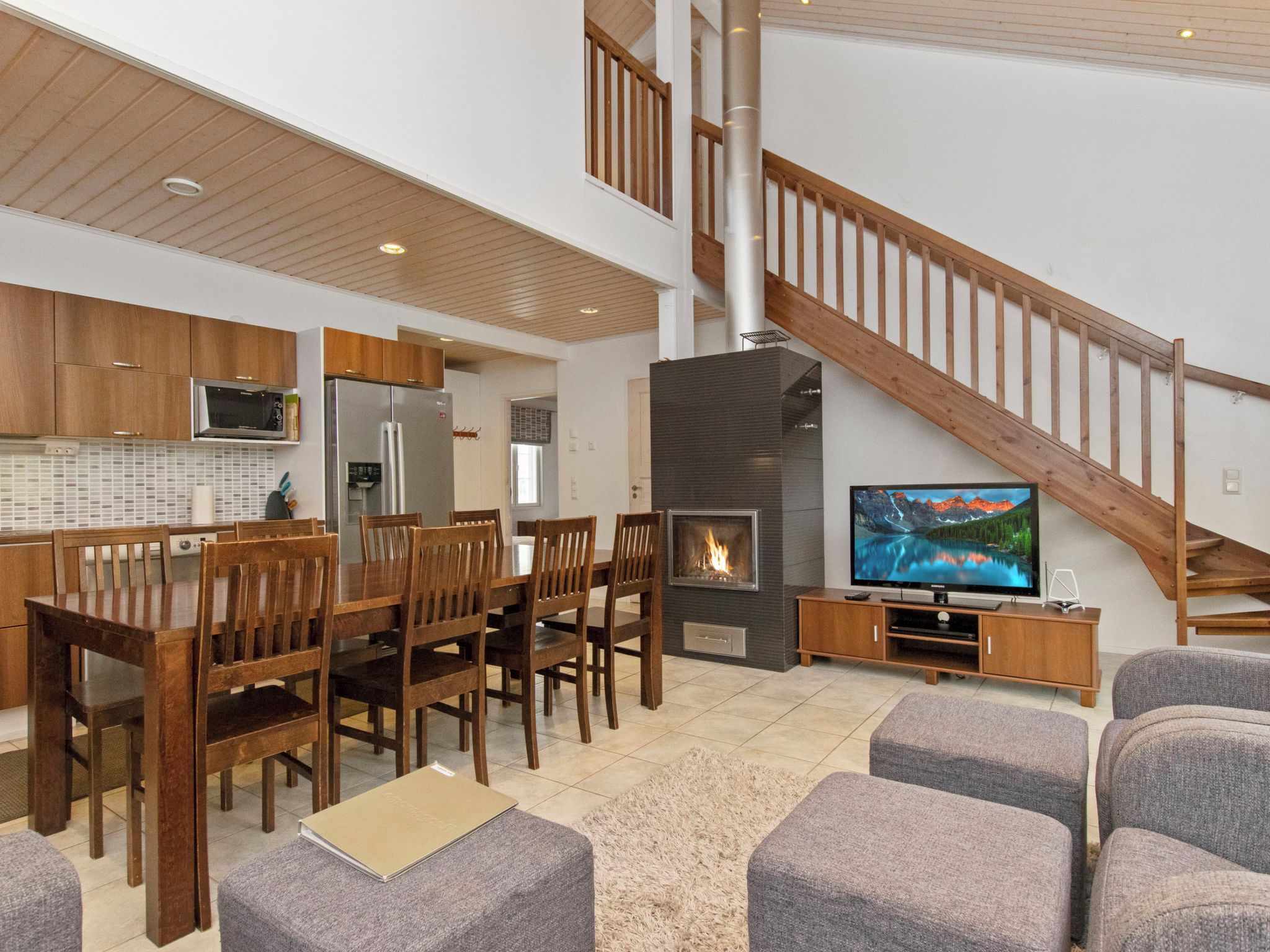 A modern living room with a fireplace, a dining area with wooden furniture, and a staircase.