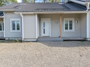 A two-story building with a grey siding exterior, a front porch, and a gravel driveway.